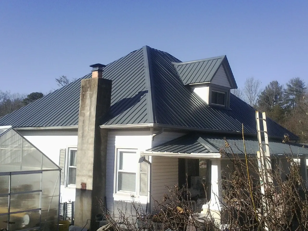 Dark blue standing seam metal roof on a white farmhouse with dormer — Slate & Tile Roof Repair by Roofing Brothers in Upper Falls