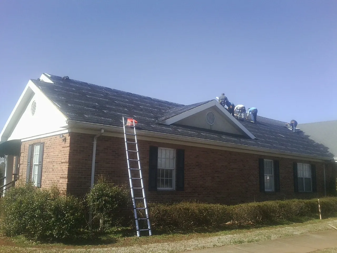 Crew tearing shingles off a brick ranch roof with a ladder set — Emergency Roof Repair work by our crew in Upper Falls