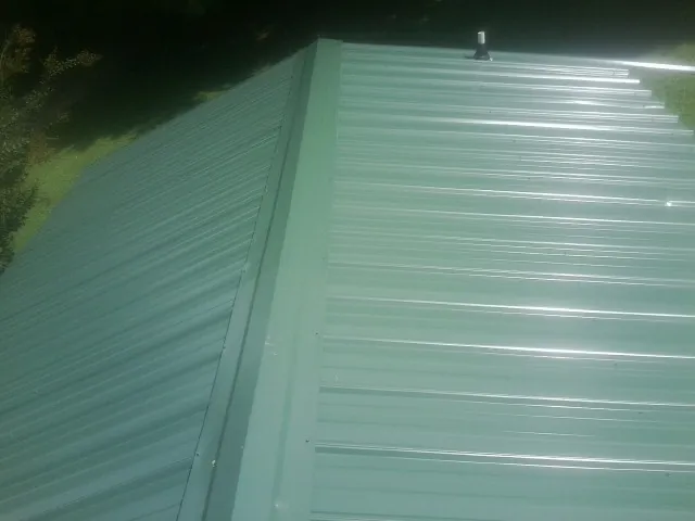 New green metal panels meeting at the ridge of a roof — Flat Roof Repair work by our crew in Upper Falls