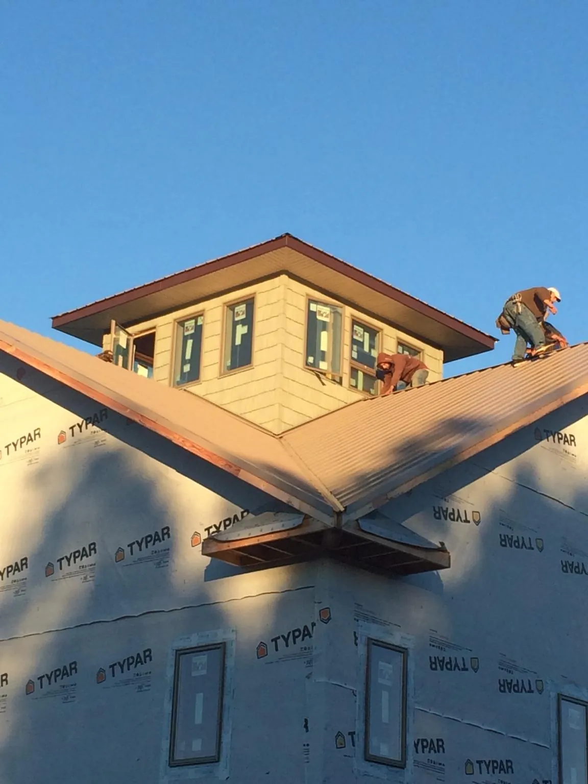 Roofers working around a rooftop cupola on a new metal roof at sunset — Roof Waterproofing in Upper Falls by Roofing Brothers